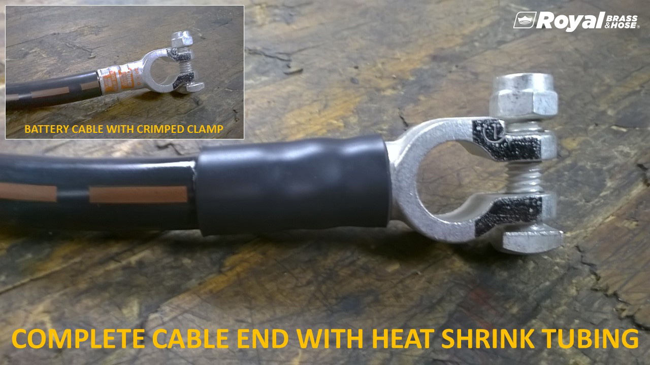 A close-up of a battery cable end with a crimped clamp, covered with heat shrink tubing. The cable end is securely attached to a metal terminal, which is designed to connect to a battery. In the upper left corner, there is a smaller inset image showing a similar battery cable with a crimped clamp. The text on the image reads, "COMPLETE CABLE END WITH HEAT SHRINK TUBING," and the logo of Royal Brass and Hose is visible in the top right corner.