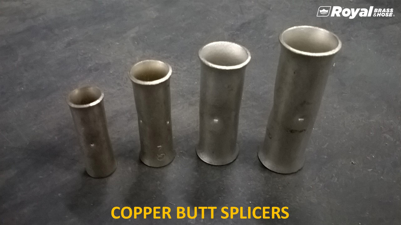  Four copper butt splicers of varying sizes arranged in a row from smallest to largest. These splicers are cylindrical and are used to connect or splice electrical cables. The text at the bottom of the image reads "COPPER BUTT SPLICERS," and the Royal Brass and Hose logo is visible in the top right corner. The background is a dark, smooth surface, highlighting the metallic appearance of the splicers.