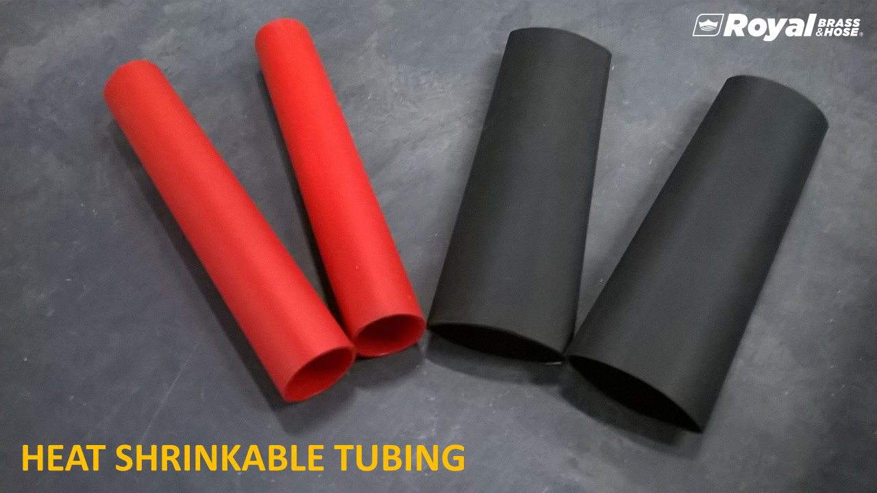 Four pieces of heat shrinkable tubing, with two in red and two in black. The tubes are cylindrical and positioned on a dark surface, slightly angled to display their hollow interiors. The text at the bottom of the image reads "HEAT SHRINKABLE TUBING," and the Royal Brass and Hose logo is visible in the top right corner.