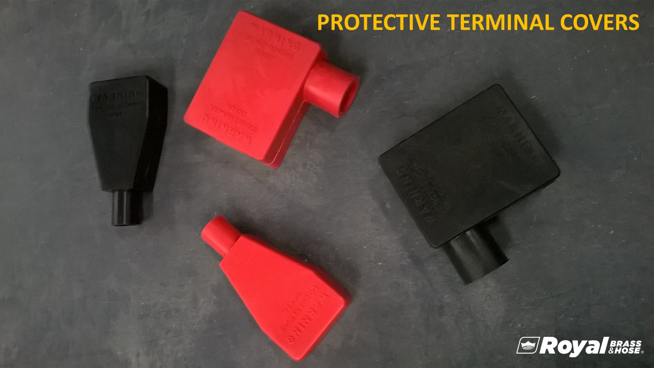 Four protective terminal covers, with two in red and two in black. These covers are designed to fit over electrical terminals to provide insulation and protection. They are arranged on a dark surface, showcasing their shape and size. The text at the top of the image reads "PROTECTIVE TERMINAL COVERS," and the Royal Brass and Hose logo is visible in the bottom right corner. The covers have warning labels molded into the material for safety information.